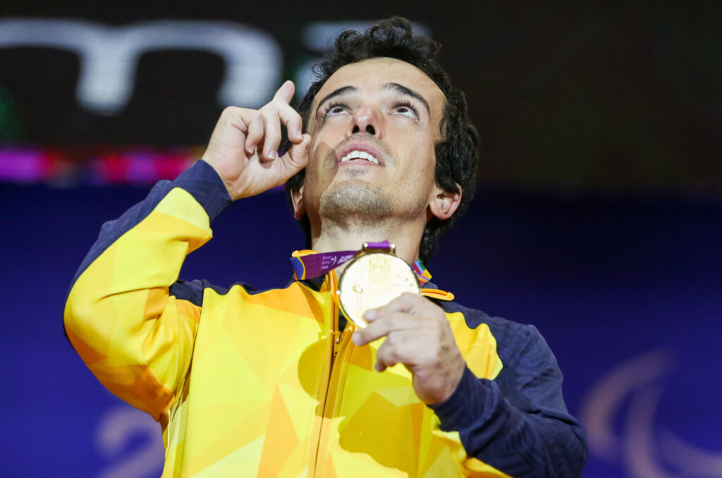 Imagem do paratleta Bruno Carra olhando para o céu em forma de agradeecimento enquanto segura uma medalha de ouro, pendurada no pescoço