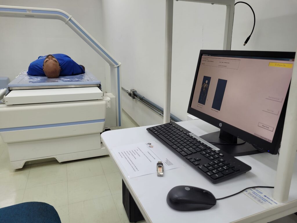 Imagem mostra o scanner DEXA com um pessoa deitada nele passando por um processo de análise